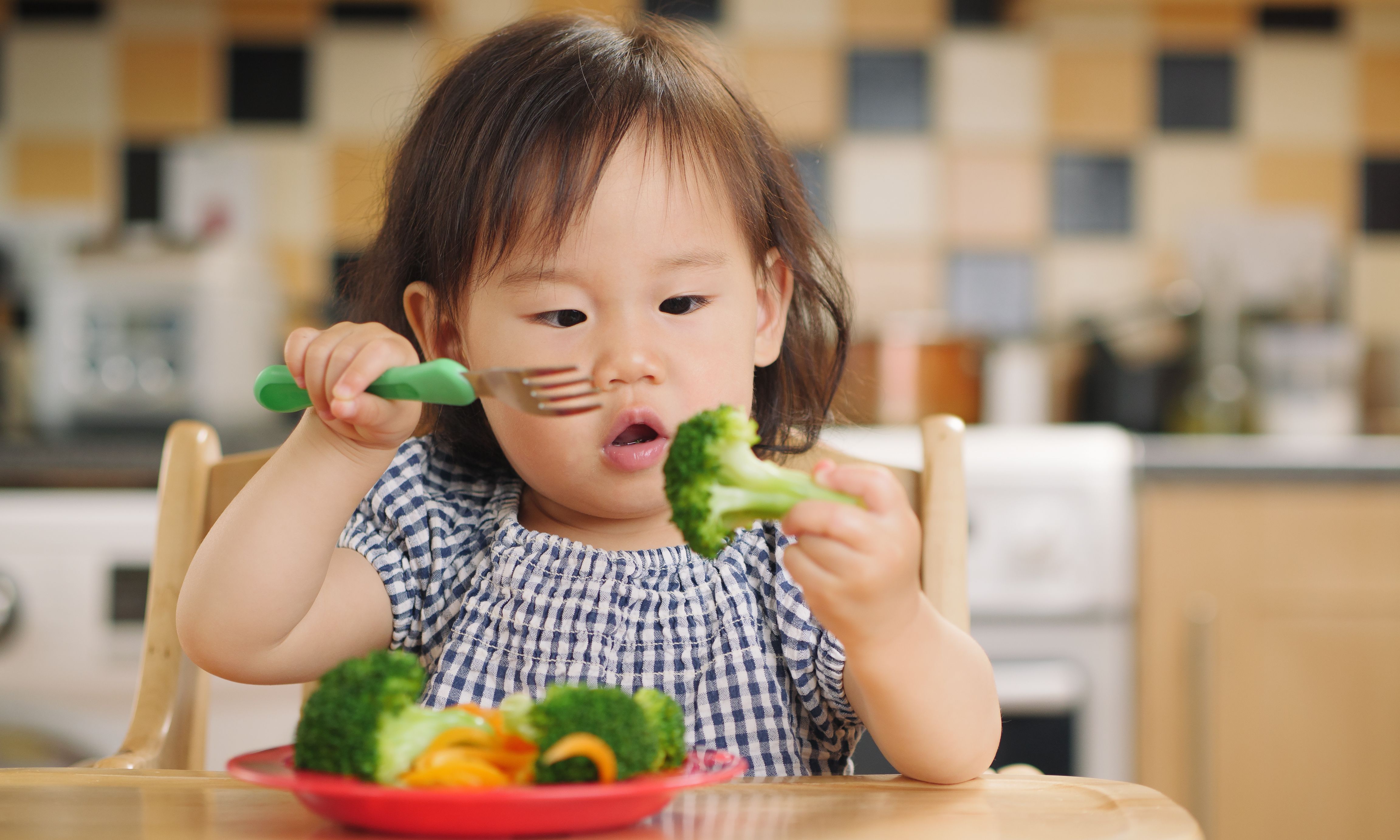Kleinkind ist Brokkolie am Tisch mit einer Gabel